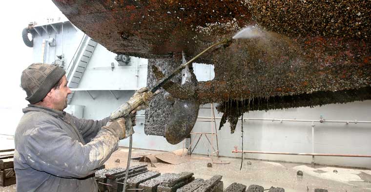 A man cleaning a boat hull with a jet wash on a dry doc