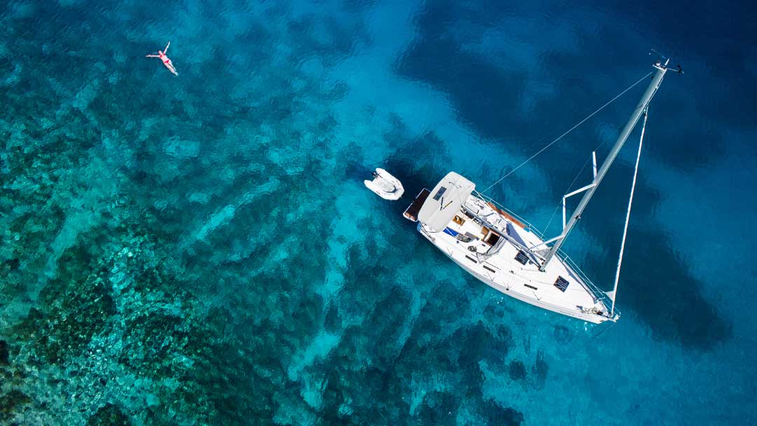 A woman in clear blue water near her yacht